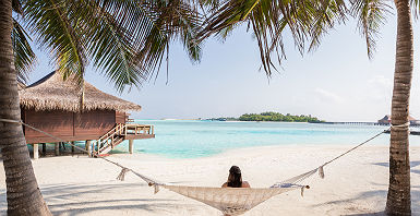 Polynésie - Portrait d'une touriste qui se repose sur une hamac avec vue sur un bungalow sur pilotis dans les eaux turquoises de Tahiti