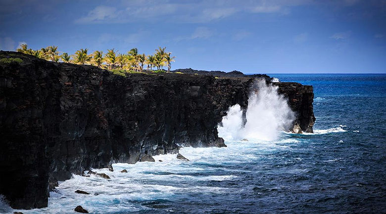 Waves crash along the black lava rock cliffs in the Hawaiian Volcanoes National Park. This view is at the end of the Chain of Craters Road