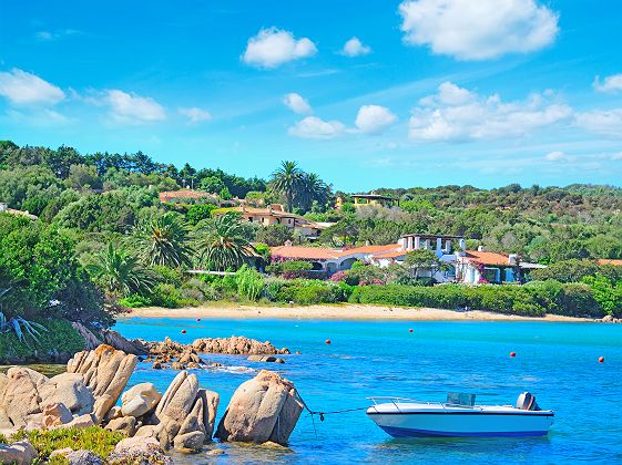 Sardaigne -  Bateau amarré à un rocher et vue sur une plage à Porto Cervo