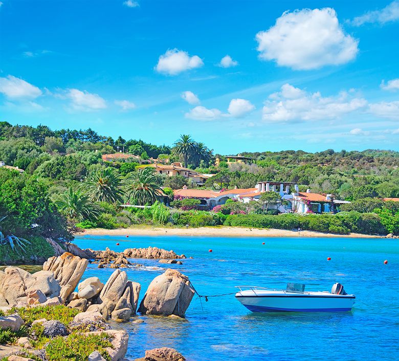 Sardaigne -  Bateau amarré à un rocher et vue sur une plage à Porto Cervo