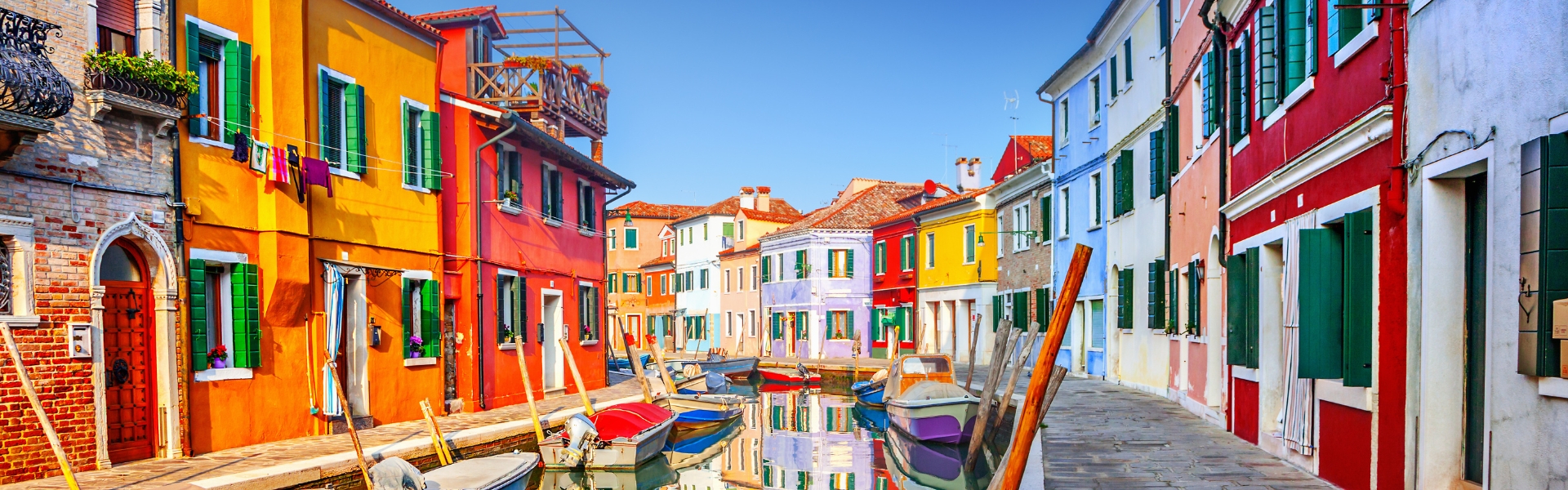 maisons colorées de burano en bordure d'un canal et ses petits bateaux sous un ciel bleu - lagune de venise